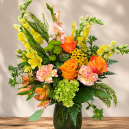 Mixed bouquet of orange roses, yellow snapdragons, and carnations in a green glass vase