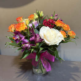 Mixed bouquet of orange roses, purple alstroemeria, and a white rose in a glass vase