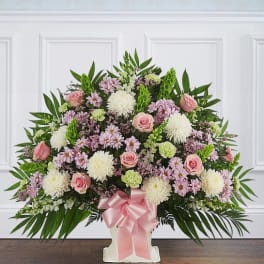 Pink and white floral spray in a white pedestal vase with a pink ribbon