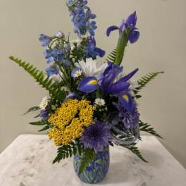 Blue and yellow mixed flower arrangement in a glass vase