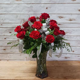 Red roses arranged in a clear glass vase with white ribbons