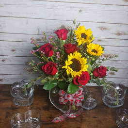 Bouquet of red roses and yellow sunflowers in a glass vase with ribbon