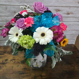 Mixed bouquet with roses, daisies, and a blue ribbon in a glass vase