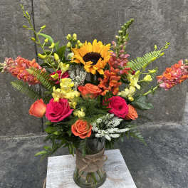 Bright mixed bouquet with sunflowers, roses, and orchids in a glass vase