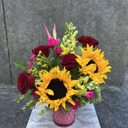 Bouquet of sunflowers, red roses, and pink flowers in a pink vase