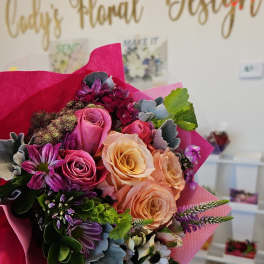 Handheld bouquet of pink, peach, and purple roses with mixed blooms