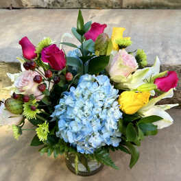 Mixed bouquet with blue hydrangea, pink roses, and yellow lilies in a glass vase