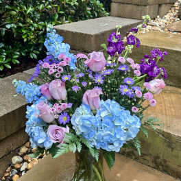 Bouquet of blue hydrangeas, pink roses, and purple flowers in a glass vase