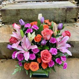 Mixed bouquet of pink lilies, roses, and orange blooms in a glass vase