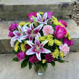Bouquet of pink roses, lilies, and yellow mums in a glass vase