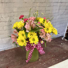 Bouquet of yellow daisies and pink alstroemeria in a green vase with a pink polka-dot ribbon