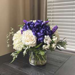 Purple and white floral arrangement in a clear glass vase