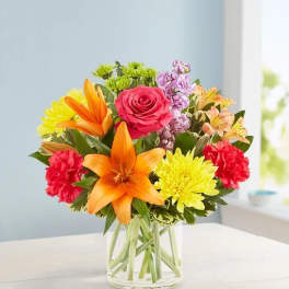 Mixed bouquet with orange lilies, pink rose, and yellow chrysanthemums in a glass vase
