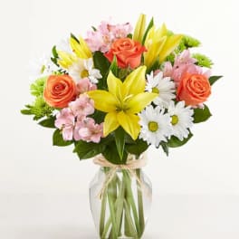 Bouquet of yellow lilies, orange roses, and white daisies in a glass vase