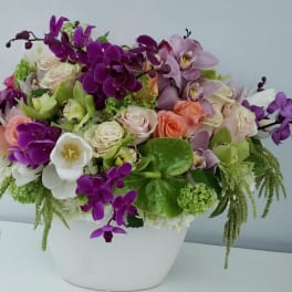 Mixed bouquet of purple orchids, roses, and white blooms in a white vase