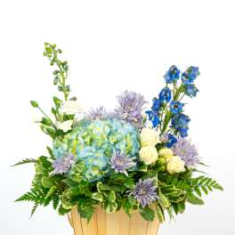 Basket arrangement with blue hydrangeas, white roses, lavender mums, and blue delphinium
