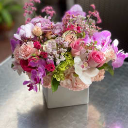 Pink and purple mixed flower arrangement in a white square vase