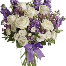 White roses and purple flowers in a glass vase with a purple ribbon