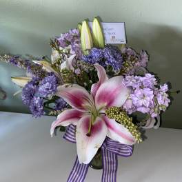 Pink lilies and lavender flowers in a glass vase with a striped ribbon