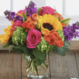 Colorful bouquet of roses, sunflowers, and purple flowers in a glass vase