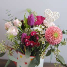 Mixed pink and purple flower arrangement in a heart-patterned mug