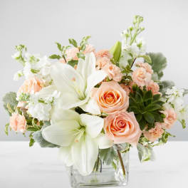 Peach roses and white lilies in a clear glass vase