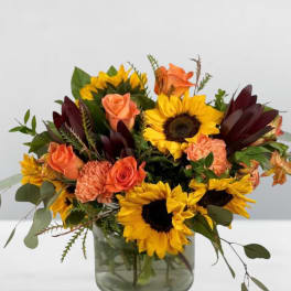 Bouquet of sunflowers, orange roses, and carnations in a glass vase