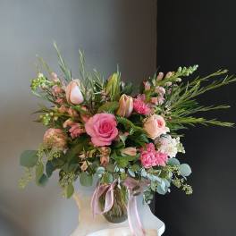 Pink and blush floral arrangement in a glass vase with a pink ribbon