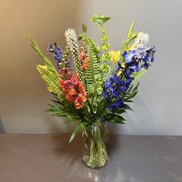 Tall mixed bouquet in a clear glass vase with blue, pink, orange, and white flowers