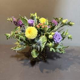 Mixed bouquet in a square glass vase with yellow, purple, and pink blooms