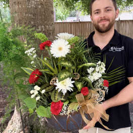 Large mixed flower arrangement in a dark bowl vase with a gold ribbon