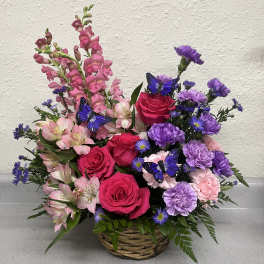 Basket arrangement of pink roses, purple carnations, and pink snapdragons with butterfly picks