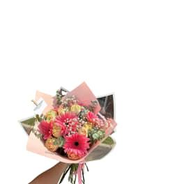 Handheld bouquet of pink gerbera daisies and peach roses wrapped in pink paper