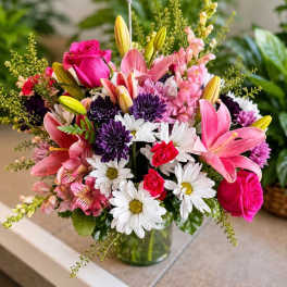 Mixed bouquet of pink lilies, roses, daisies, and purple blooms in a glass vase