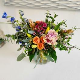 Mixed bouquet with orange roses, pink blooms, and blue flowers in a glass vase