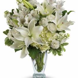 White lilies and mixed white flowers in a clear glass vase