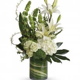 Tall white lilies, roses, and hydrangeas with green accents in a leaf-lined glass cylinder vase