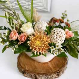 Low arrangement of peach roses, white rose, yellow chrysanthemum and white pods in a bowl vase