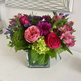 Pink and purple mixed flower arrangement in a square glass vase
