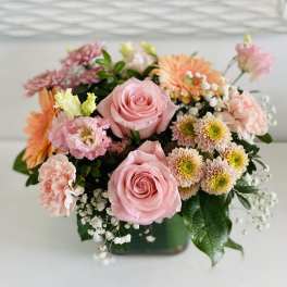 Pink roses and mixed pastel flowers arranged in a low square vase
