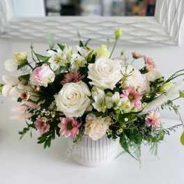 Low white ceramic vase filled with white roses, pink daisies, and soft pastel mixed flowers.