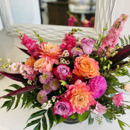 Bright arrangement of pink and orange dahlias, roses, snapdragons, and mums in a low glass vase