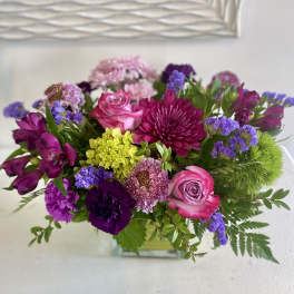 Mixed bouquet of pink, purple, and yellow flowers in a glass vase