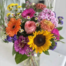 Bright mixed bouquet with sunflower, gerbera daisies, and a rose in a clear glass vase