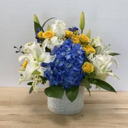 Blue hydrangea and white lilies with yellow roses in a white vase