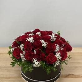 Red roses arranged in a round black box with white filler flowers