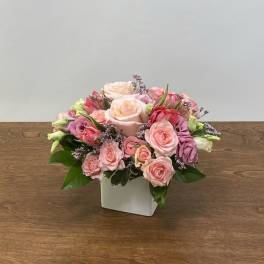 Pink and peach roses arranged in a white square vase