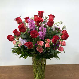 Red roses and pink flowers arranged in a clear glass vase