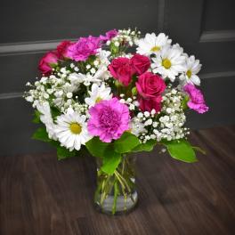 Bouquet of pink roses, white daisies, and pink carnations in a glass vase