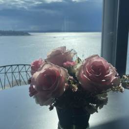 Pink rose bouquet in a small glass vase on a table by a window